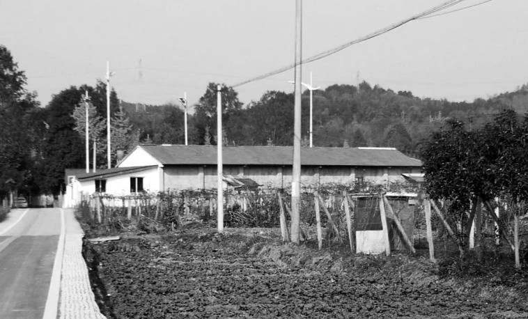 Black and white archival photograph of the low village school beside a road and fields