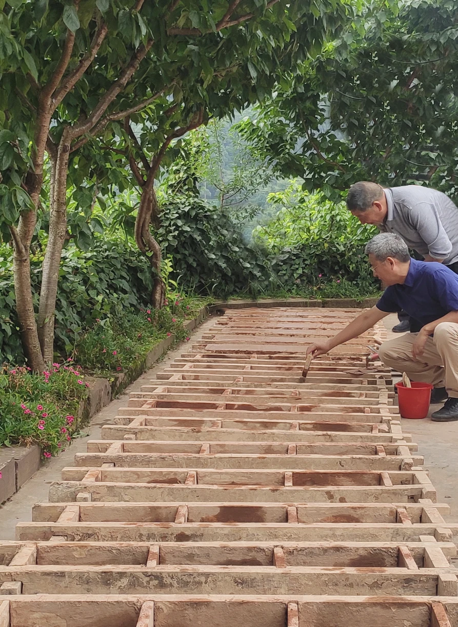 Two people working beside rows of timber brick moulds at Xingfu Ridge